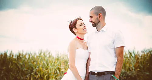 My husband and I in a cornfield, wearing my mother's altered wedding dress — (almost) the same dress, a few decades later
